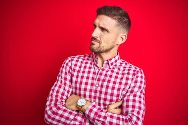 Genç ve yakışıklı bir adam, izole edilmiş, kollarını kavuşturmuş, kendinden emin ve ikna olmuş bir şekilde yan tarafa bakıyor.