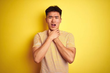 Asyalı genç bir Çinli tişört giyip izole edilmiş sarı arka planda dikilmiş bağırıyor ve boğuluyor çünkü acı verici bir boğulma var. Sağlık problemi. Boğulma ve intihar konsepti.