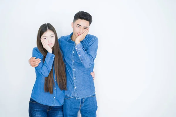 Beautiful young asian couple over white isolated background thinking looking tired and bored with depression problems with crossed arms.
