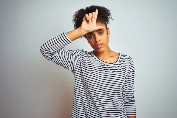 African american woman wearing navy striped t-shirt standing over isolated white background making fun of people with fingers on forehead doing loser gesture mocking and insulting.
