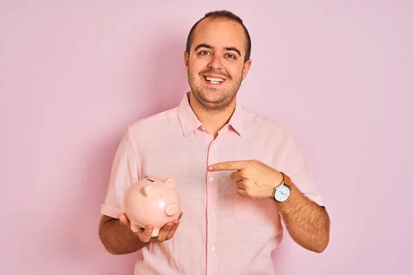 Jovem Segurando Piggybank Sobre Fundo Rosa Isolado Muito Feliz Apontando — Fotografia de Stock