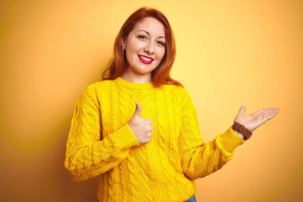 美丽的红头发女人 穿着冬季毛衣 站在孤立的黄色背景上 手举着手 竖起大拇指 做着一个还好的手势 笑容满面 开朗愉快 — 图库照片