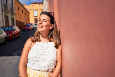 Turuncu duvara yaslanan güzel kız, güneşli bir yaz gününde gülümseyen genç arkadaş.