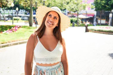 Genç ve güzel bir kadın mutlu bir şekilde gülümsüyor güneşli bir yaz gününde şehir sokaklarında yürüyor.