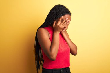 Kırmızı günlük tişört giyen Afro-Amerikalı kadın izole edilmiş sarı arka planda dikiliyor ve ağlarken suratını ellerle kapatıyor. Depresyon kavramı.