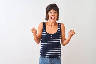 İzole edilmiş beyaz arka plan üzerinde duran çizgili tişört giyen genç ve güzel bir kadın kollarını kaldırarak ve açık gözlerle başarıyı kutluyor ve şaşırıyor. Kazanan konsept.