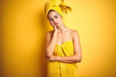 Vücuduna ve başına duş havlusu takan güzel bir kadın izole edilmiş sarı arka planda yorgun ve bunalımda kollarını kavuşturmaktan sıkılmış görünüyor..