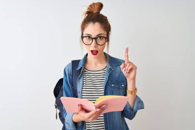 Sırt çantası takan kızıl saçlı kız izole edilmiş beyaz arka plan üzerine kitap okuyor. Bir fikir ya da soru işareti ile şaşırıyor.