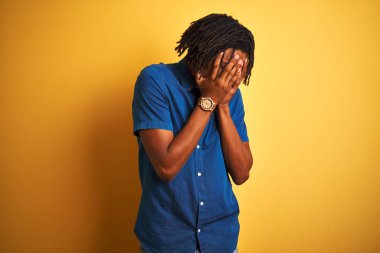 Rastgele kot gömlek giyen Afro bir adam izole edilmiş sarı arka planda duruyor ve ağlarken suratını ellerle kapatıyor. Depresyon kavramı.