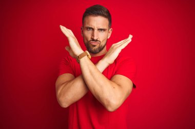 Kırmızı izole edilmiş arka plan üzerine gündelik tişört giyen genç yakışıklı adam. Reddedilmiş yüz ifadesi.