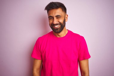 Genç Hintli bir adam pembe arka planda dikilip kameraya seksi bir ifadeyle bakıyor, neşeli ve mutlu bir yüzle..