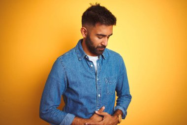 Kotlu gömlek giyen genç Hintli adam midesi bulanan, acı verici bir hastalıktan dolayı izole edilmiş sarı arka planda duruyor. Ache kavramı.