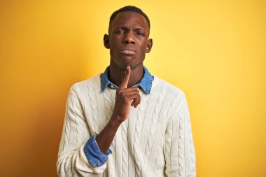 İzole edilmiş sarı arka planda kot gömlek ve beyaz süveter giyen Afro-Amerikan bir adam parmak çenede ve yukarı bakarak şüphe üzerine yoğunlaşmıştı.