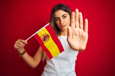 İspanyol bayrağını kırmızı izole arka planda tutan genç ve güzel bir kadın. Açık elle dur işareti yapıyor. Ciddi ve kendinden emin bir ifadeyle, savunma jesti.