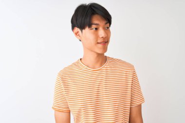 Sıradan çizgili tişört giyen genç Çinli bir adam izole edilmiş beyaz arka planda dikilip yüzünde gülümseme, doğal bir ifade ile yan yana bakıyor. Kendinden emin gülen.