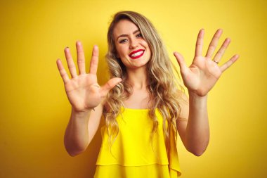 Sarı arka planda duran tişörtlü genç saldırgan kadın on numaralı parmaklarıyla işaret ederken kendinden emin ve mutlu bir şekilde gülümsüyor..