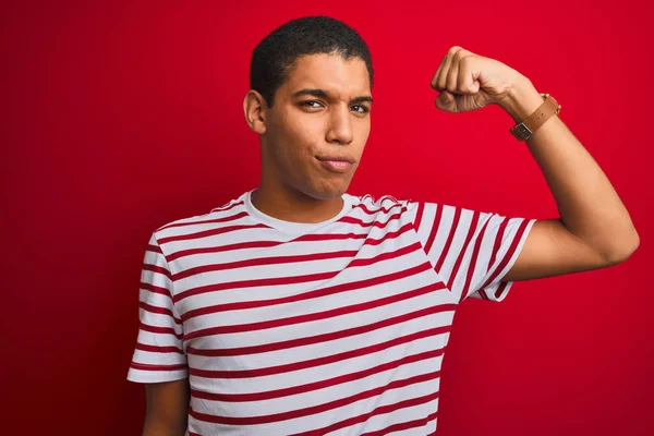 年轻英俊的阿拉伯男子 身穿条纹T恤 身披孤立的红色背景 强壮的人展示臂膀肌肉 自信而自豪 — 图库照片