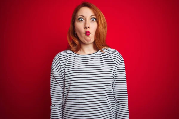 若い赤毛の女性は 狂気とコミカルなジェスチャーで魚の顔を作る赤い隔離された背景の上に立って海軍のシャツを身に着けている 面白い表現 — ストック写真