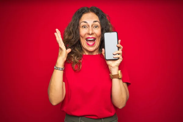 赤の孤立した背景にスマートフォンの画面を示す中年のシニア女性は非常に幸せと興奮 大きな笑顔で叫んで勝利を祝う勝者式と手を上げ — ストック写真
