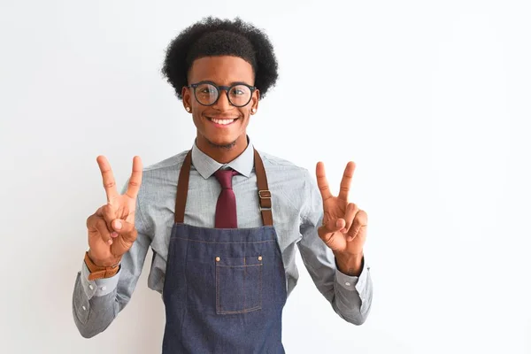 年轻的非洲裔美国店主 戴着围裙眼镜 站在孤立的白色背景上 微笑着看着摄像机 手指头在做胜利的标志 第二点 — 图库照片