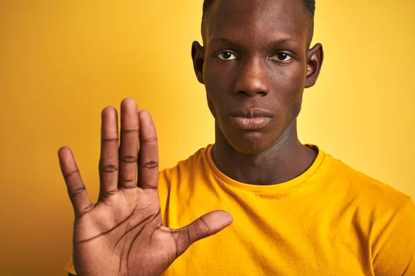 アフリカ系アメリカ人の男を着てカジュアルTシャツの上に立って孤立した黄色の背景で手を開いて停止記号を行うと深刻で自信を持って式 防衛ジェスチャー — ストック写真
