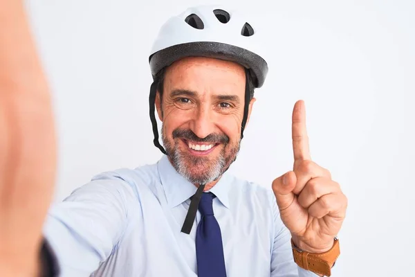 Middle age businessman wearing bike helmet make selfie over isolated white background surprised with an idea or question pointing finger with happy face, number one