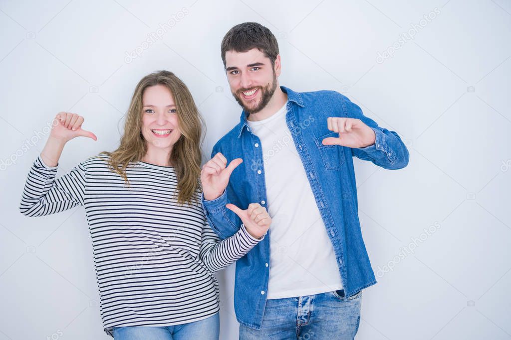 Young beautiful couple standing together over white isolated background looking confident with smile on face, pointing oneself with fingers proud and happy.
