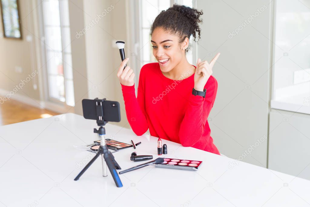 Young african american influencer woman recording make up tutorial very happy pointing with hand and finger to the side
