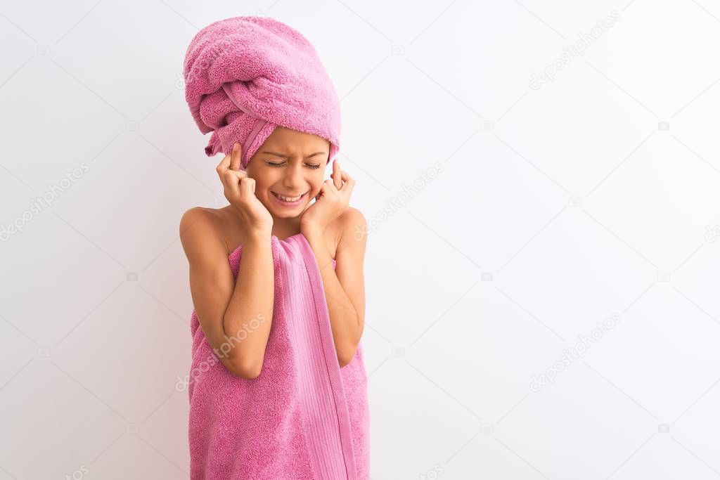Beautiful child girl wearing shower towel after bath standing over isolated white background gesturing finger crossed smiling with hope and eyes closed. Luck and superstitious concept.