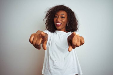 Genç Afro-Amerikan kadın tişört giyip izole edilmiş beyaz arka planda dikiliyor. Sana ve kameraya parmaklarıyla bakıyor.