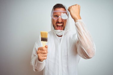 Profesyonel işçi ekipmanı giyen ressam arka planda fırça tutuyor. Öfkeyle bağırıyor, sinirleniyor ve sinirleniyor. Öfkeyle bağırıyor.