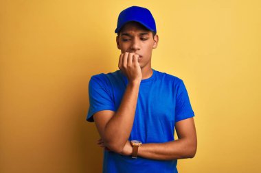 Yakışıklı Arap teslimatçı, izole edilmiş sarı arka planda duruyor. Ağzı tırnak ısıran ellerle stresli ve gergin görünüyor. Endişe sorunu.