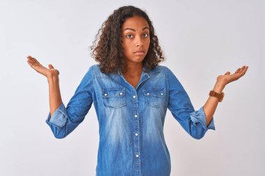 İzole edilmiş beyaz arka plan üzerinde duran Brezilyalı genç bir kadın kolları ve elleri havada, kafası karışmış bir ifade takınıyor. Şüphe kavramı.