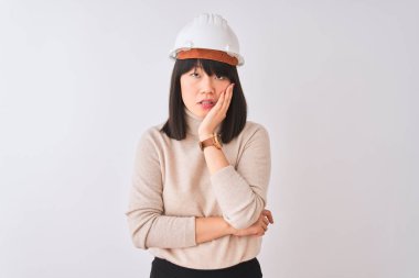 Genç, güzel bir Çinli mimar kadın, kask takıp izole edilmiş beyaz arka planda yorgun ve bunalımda kollarını kavuşturmaktan sıkılmış görünüyor..