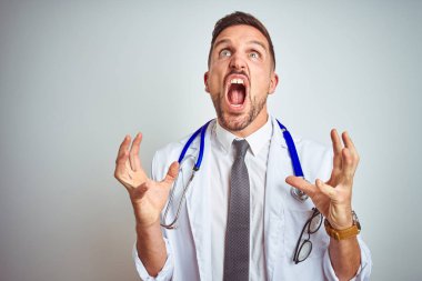 İzole edilmiş arka plan üzerinde beyaz profesyonel ceket giyen genç yakışıklı doktor kızgın ve deli gibi bağırıyor ve agresif bir ifade ve kollarla bağırıyor. Hayal kırıklığı konsepti.