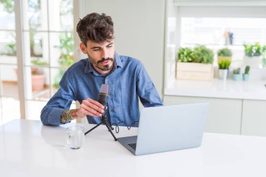 Genç adam podcast 'i mikrofon ve dizüstü bilgisayarla kaydediyor.