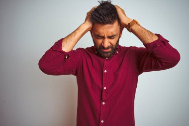 Kırmızı şık gömlek giyen genç Hintli adam izole edilmiş gri arka planda duruyor. Ağrı ve migren yüzünden baş ağrısı ve stresten muzdarip. Ellerini başının üstüne koy..