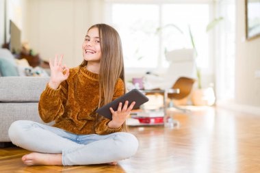 Güzel genç kız çocuk parmak ile ok işareti yapıyor katta oturan dijital Touchpad tablet kullanarak, mükemmel sembolü