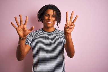 Rastalı Afro adam, donanma çizgili tişört giyiyor. İzole edilmiş pembe arka plan üzerinde duruyor. Sekiz numarayı işaret ediyor..