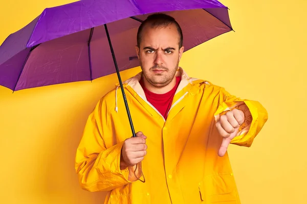 Junger Mann Regenmantel Mit Lila Regenschirm Vor Isoliertem Gelben Hintergrund — Stockfoto