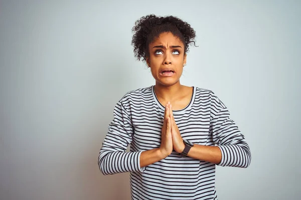 African american woman wearing navy striped t-shirt standing over isolated white background begging and praying with hands together with hope expression on face very emotional and worried. Asking for forgiveness. Religion concept.