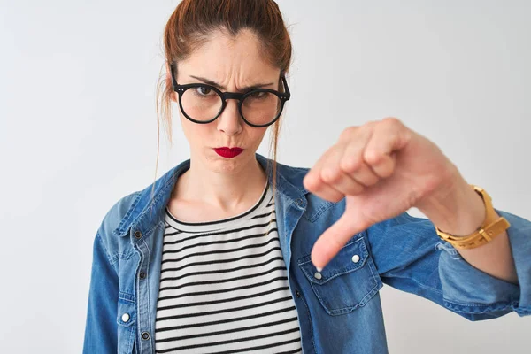 Redhead woman wearing denim shirt and glasses standing over isolated white background with angry face, negative sign showing dislike with thumbs down, rejection concept
