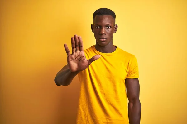 年轻的非洲裔美国人穿着休闲的T恤 站在孤立的黄色背景上 停止手心唱着歌 脸上带有消极而严肃的手势的警告表情 — 图库照片