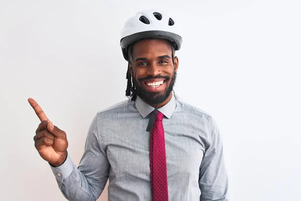 African american businessman with braids wearing bike helmet over isolated white background with a big smile on face, pointing with hand and finger to the side looking at the camera.