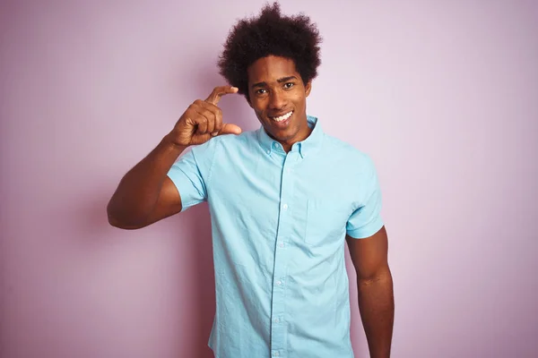 青いシャツを着たアフロの髪をした若いアメリカ人男性がピンクの背景の上に立ち 指を見てカメラで小さなサイズの看板をして手で笑顔と自信を持ってジェスチャー 概念の測定 — ストック写真