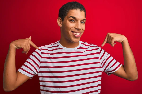 年轻英俊的阿拉伯男子穿着条纹T恤 披着孤立的红色背景 面带微笑 带着自信 用手指指着自己 自豪而快乐 — 图库照片