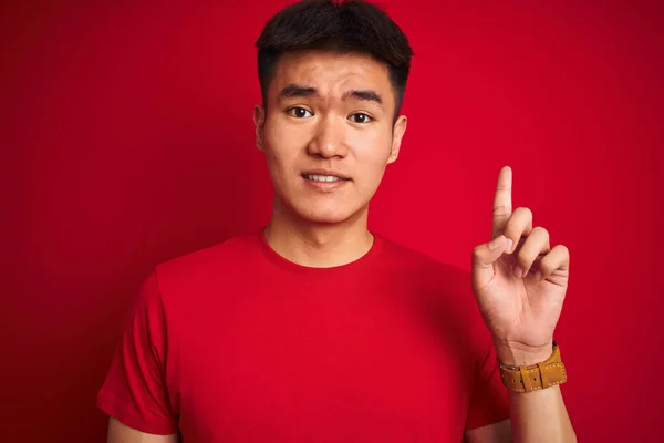 若いですアジアの中国人男性身に着けているTシャツ上に立って孤立した赤い背景驚きでアイデアや質問を指差す指で幸せな顔 ナンバーワン — ストック写真