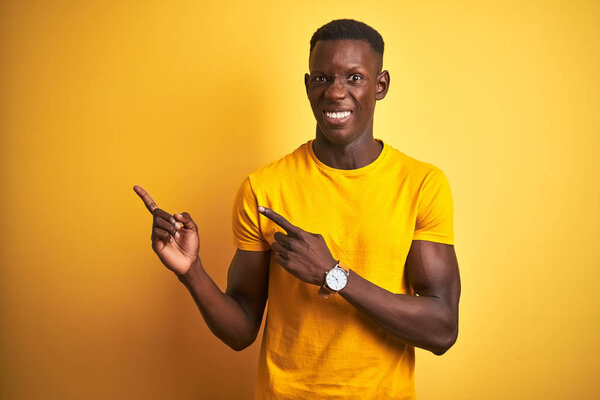 Young african american man wearing casual t-shirt standing over isolated yellow background Pointing aside worried and nervous with both hands, concerned and surprised expression