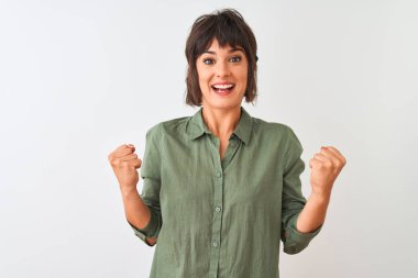 Yeşil gömlekli genç bir kadın izole edilmiş beyaz arka planda dikilmiş şaşırmış ve şaşırmış bir şekilde kollarını kaldırarak ve gözlerini açarak başarıyı kutluyor. Kazanan konsept.