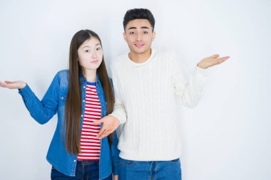 Beyaz, soyutlanmış arka planda yaşayan genç ve güzel Asyalı bir çift. Kolları ve elleri havada, kafası karışmış bir ifade. Şüphe kavramı.
